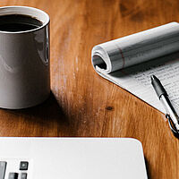 Notepad with Pen on Top Next to a Mug of Coffee