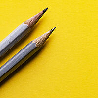 two grey led pencils sitting on a yellow background